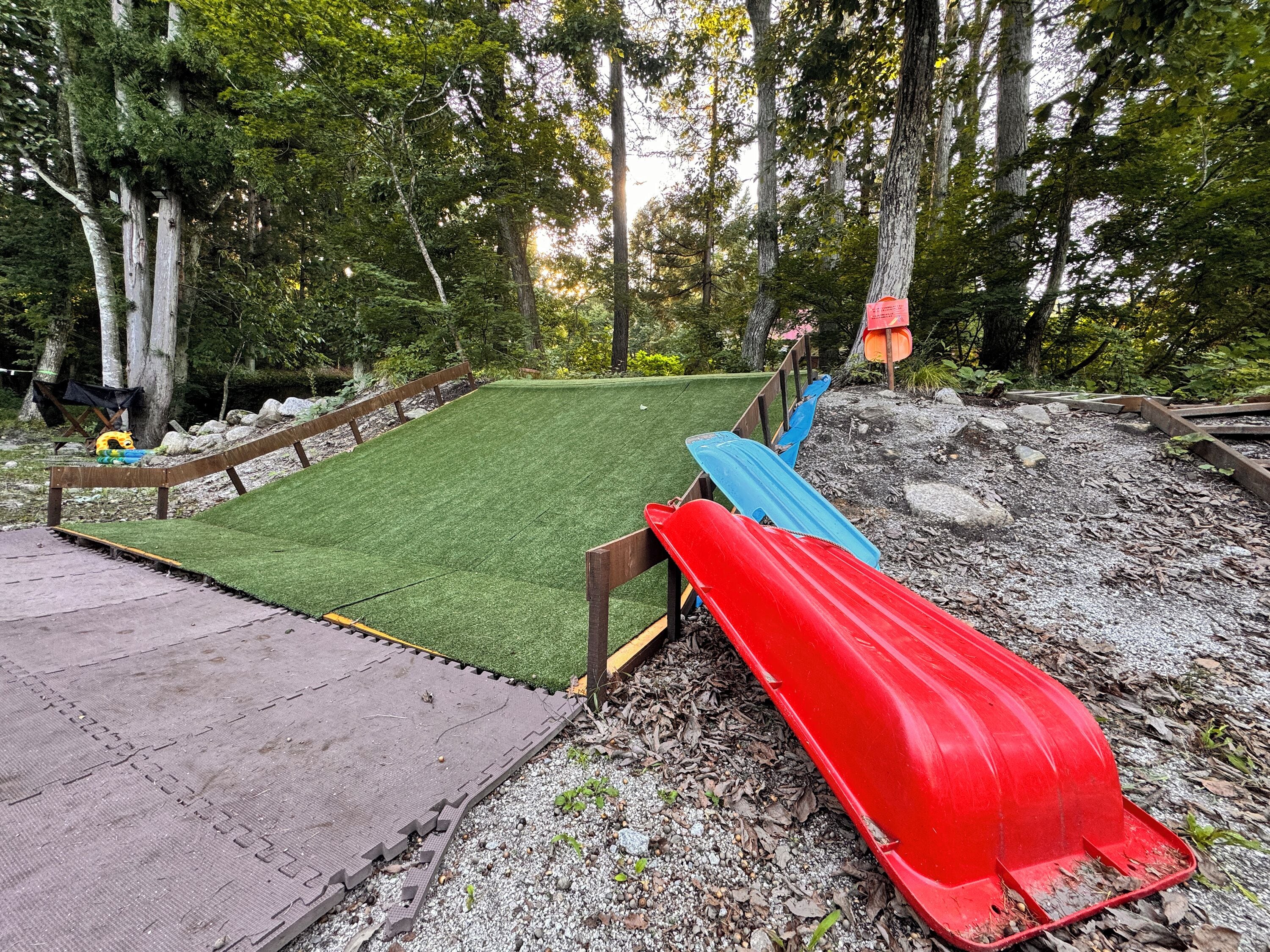 A backyard with artificial grass, a red slide, and a blue slide.
