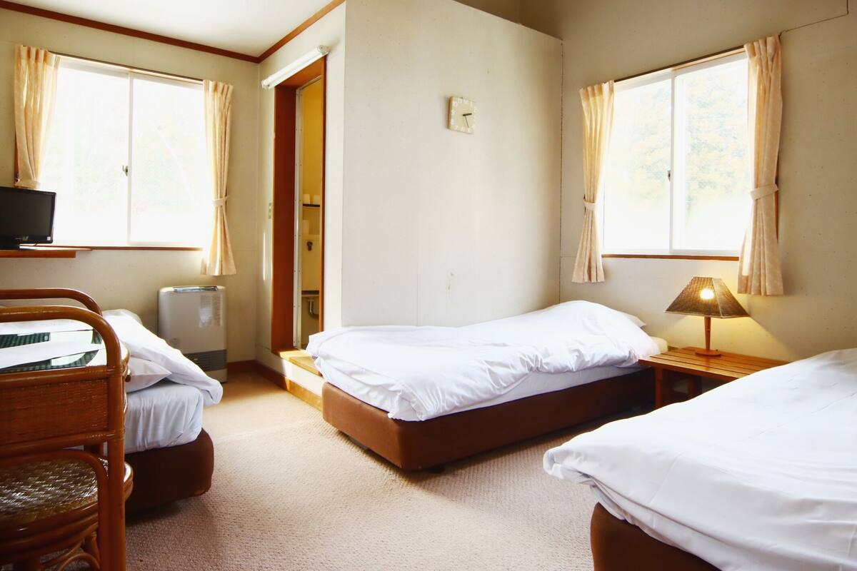 A room with two beds, a desk, a chair, and a lamp.
