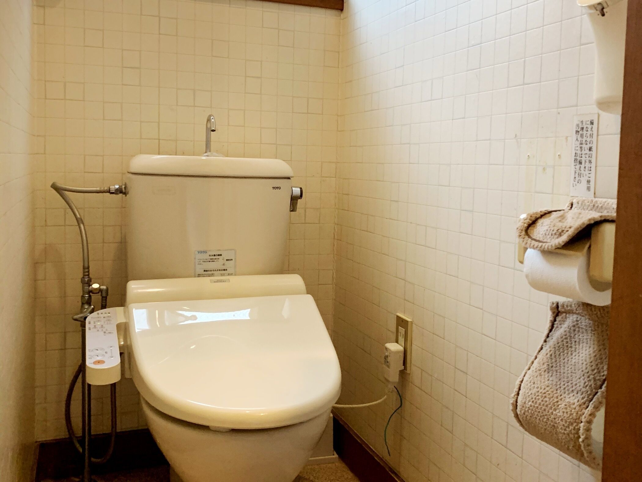 Un baño pequeño y limpio con inodoro, cabezal de ducha manual y una toalla colgada en un gancho.