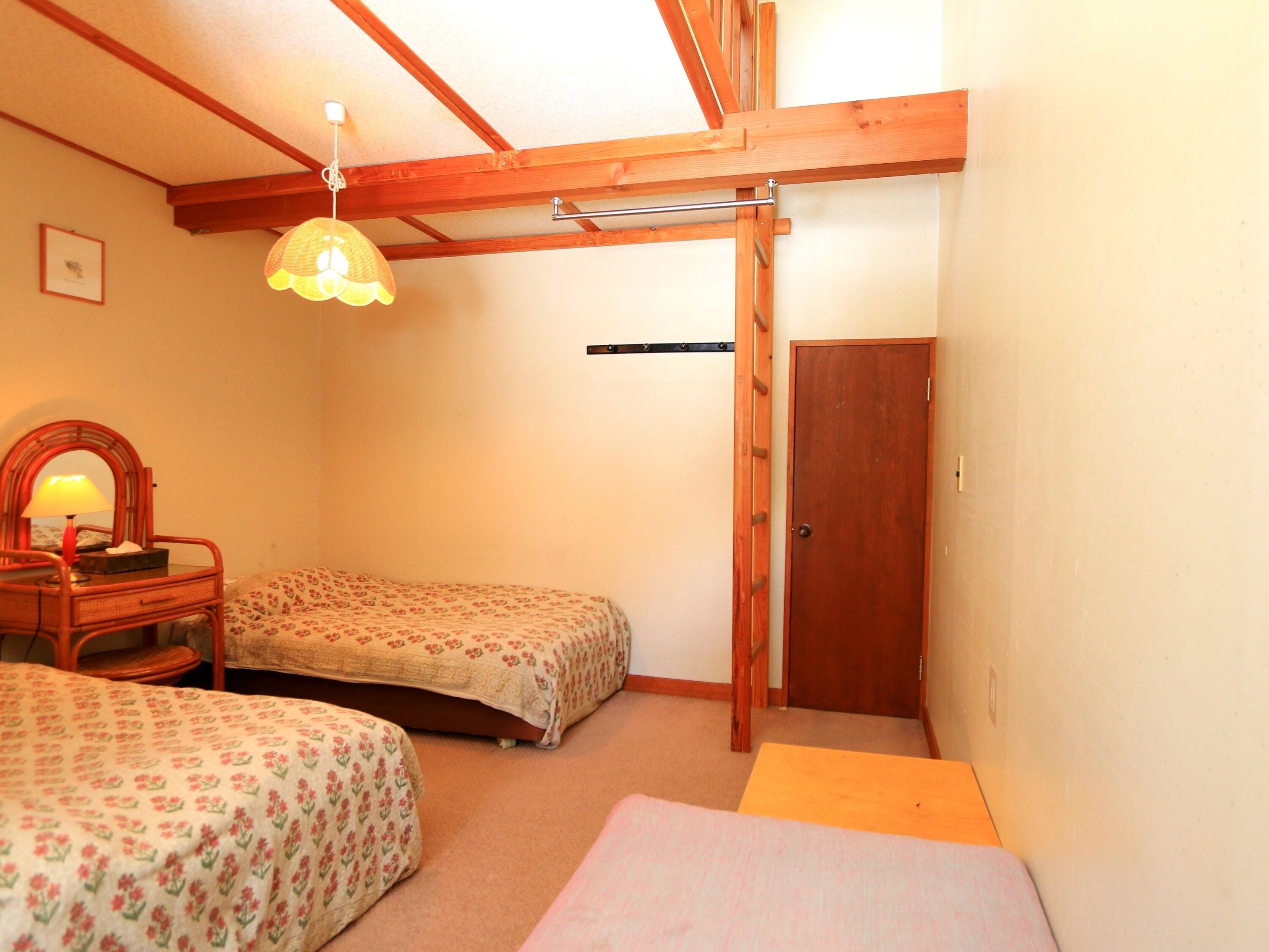 A room with two single beds, a wooden ceiling, a door, and a hanging lamp.