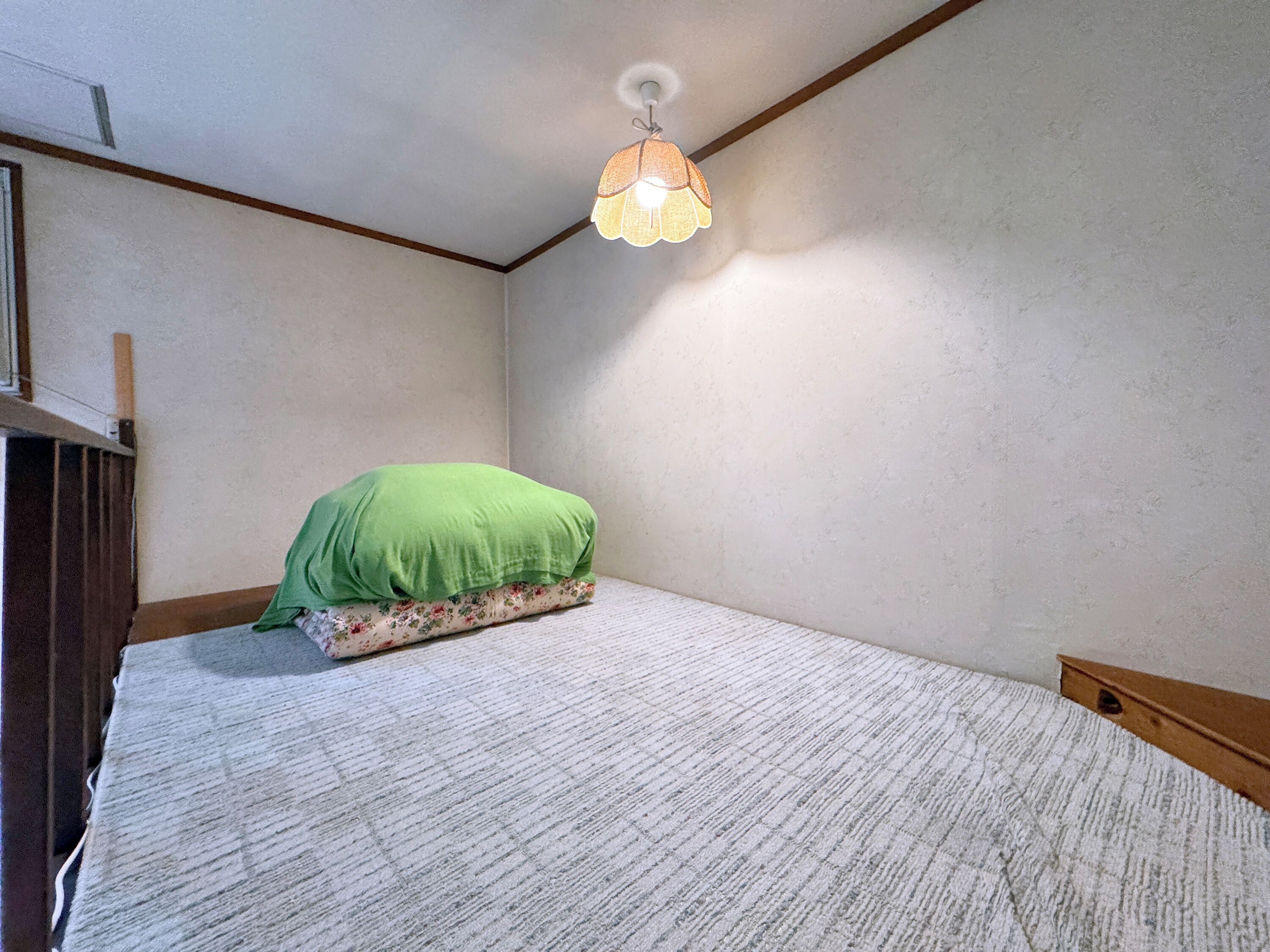A small, single-bed room with a green pillow and a patterned bedspread.