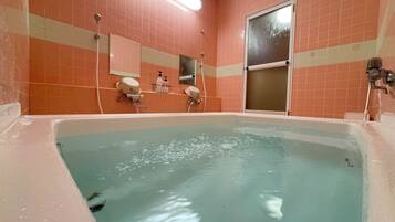 A bathroom with a large bathtub, a mirror, and a shower area.