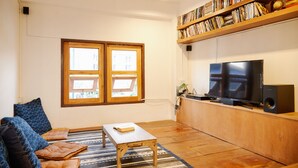 Una sala de estar con piso de madera, un sofá, una mesa de centro, una estantería y un televisor.