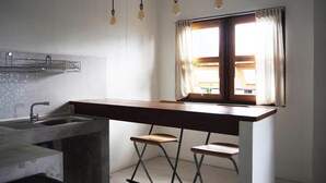 Una cocina compacta con un lavamanos integrado, una ventana con cortinas y un taburete de bar.