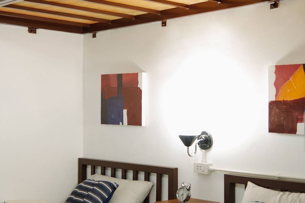A bedroom with two beds, a wooden ceiling, and abstract wall art.