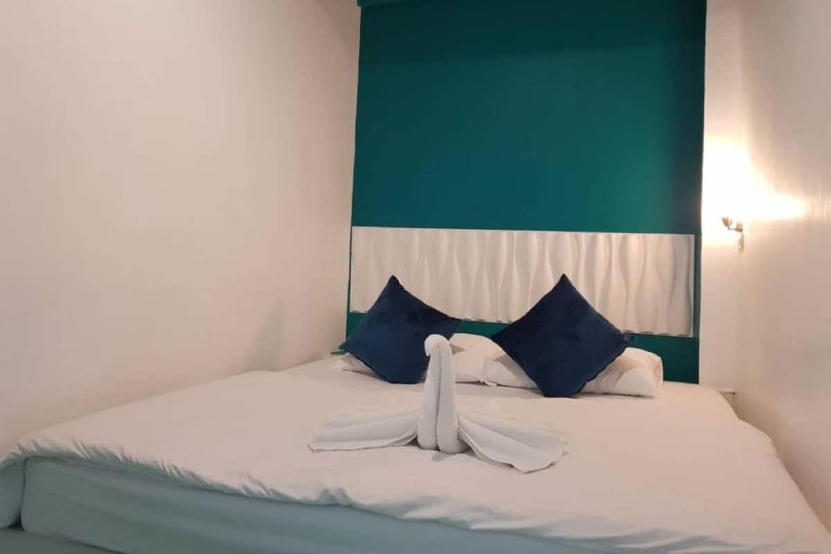 Una cama bien hecha con almohadas blancas y azules, un cabecero verde azulado y un arreglo de toallas sobre la cama.