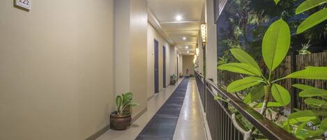 A corridor with a number sign, potted plants, and a railing with greenery.