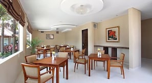 Un comedor de hotel con varias mesas y sillas de madera, una chimenea y un gran ventanal con cortinas.