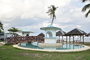 A pool area with a bridge, palm trees, and thatched-roof structures. - King Arthur's Place (Alcoy)