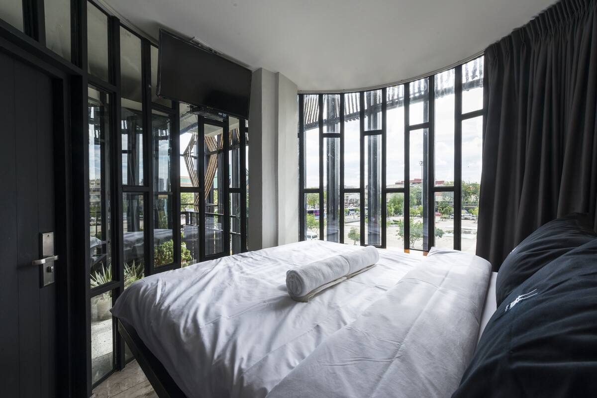 Une chambre avec un grand lit, une télévision et une vue sur le paysage urbain, grâce à de grandes fenêtres.