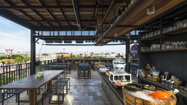 An outdoor bar area with tables and chairs, a large ice bucket with a carved pig, and shelves with bottles and glasses. - Chingcha Bangkok - Hostel (Bangkok)