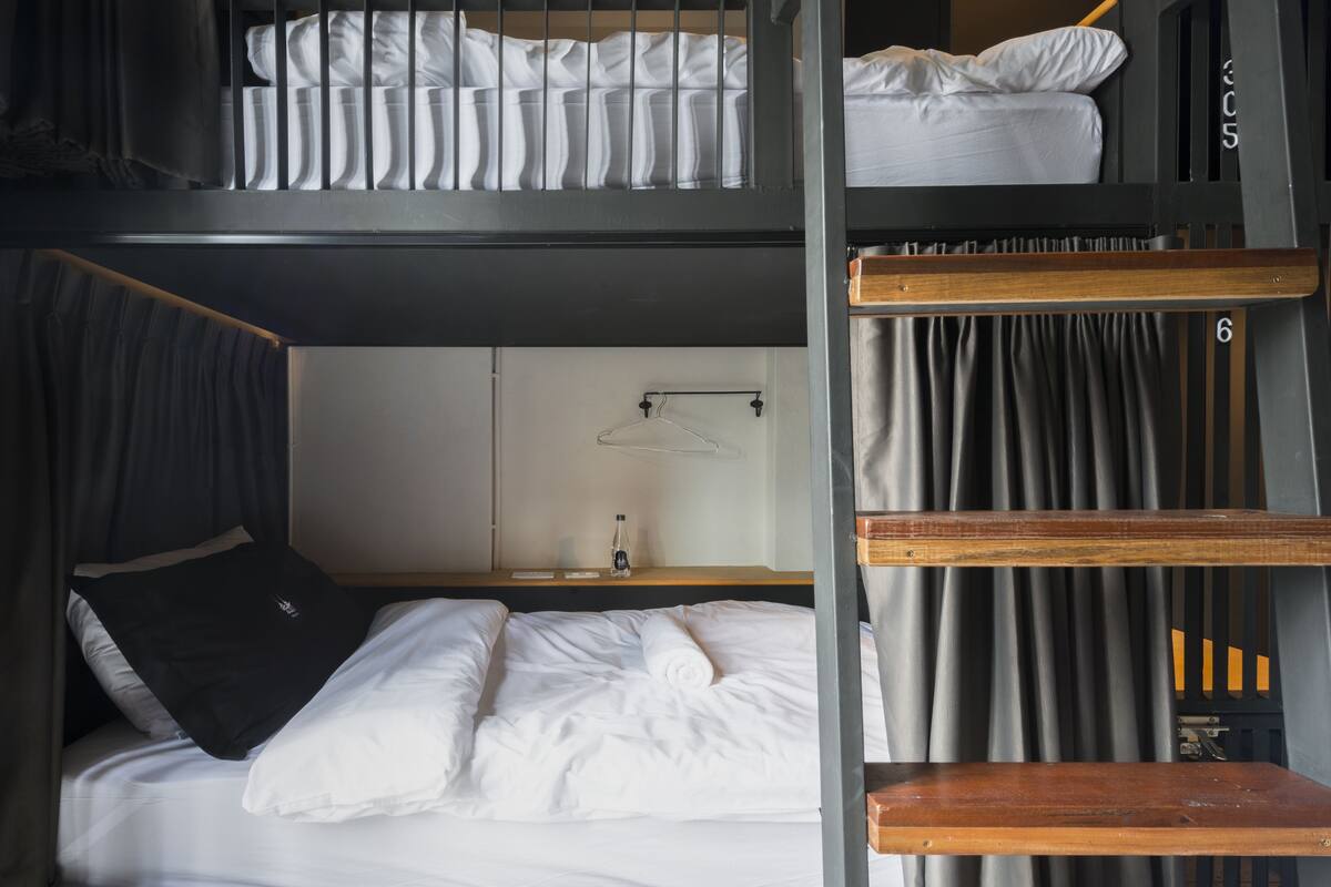 Une chambre avec un lit superposé, un bureau en bois, une lampe suspendue et un rideau.