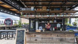 A bar with a wooden counter, shelves with bottles, and a chalkboard menu. - Chingcha Bangkok - Hostel (Bangkok)