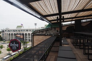 A restaurant with a view of a building with a flag, a signboard, and outdoor seating. - Chingcha Bangkok - Hostel (Bangkok)