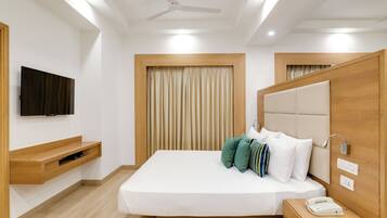 A modern hotel room with a bed, a TV, a bedside table with a phone, and a ceiling fan.