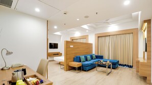 A modern hotel room with a wooden desk, a blue sofa, a small coffee table, and a TV mounted on the wall. - Lemon Tree Hotel, Sector 60, Gurugram (Sohna)