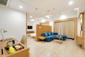 A modern hotel room with a wooden desk, a blue sofa, a small coffee table, and a TV mounted on the wall. - Lemon Tree Hotel, Sector 60, Gurugram (Sohna)