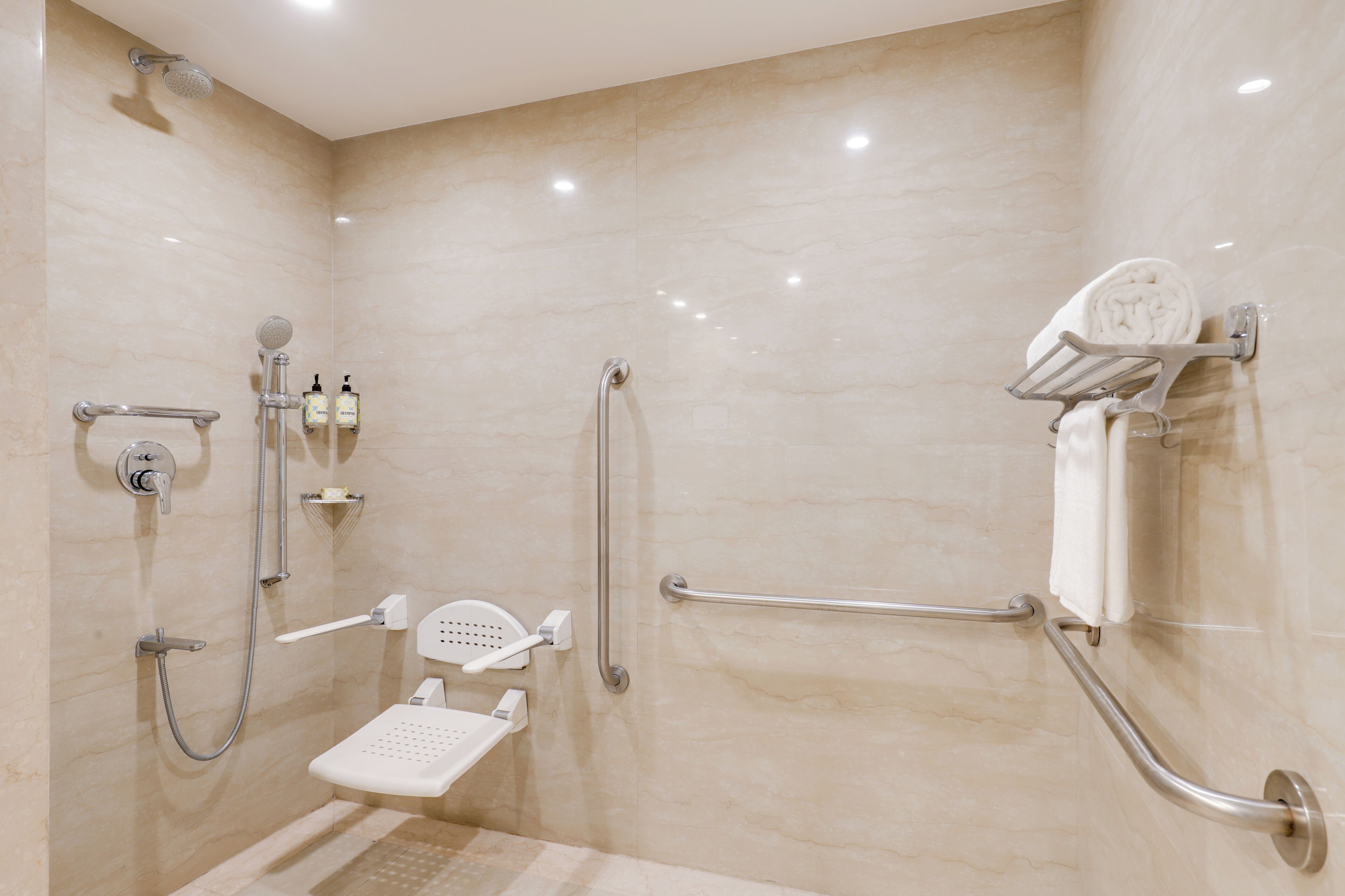 Un baño con ducha, barras de apoyo, toallero y dispensador de jabón.