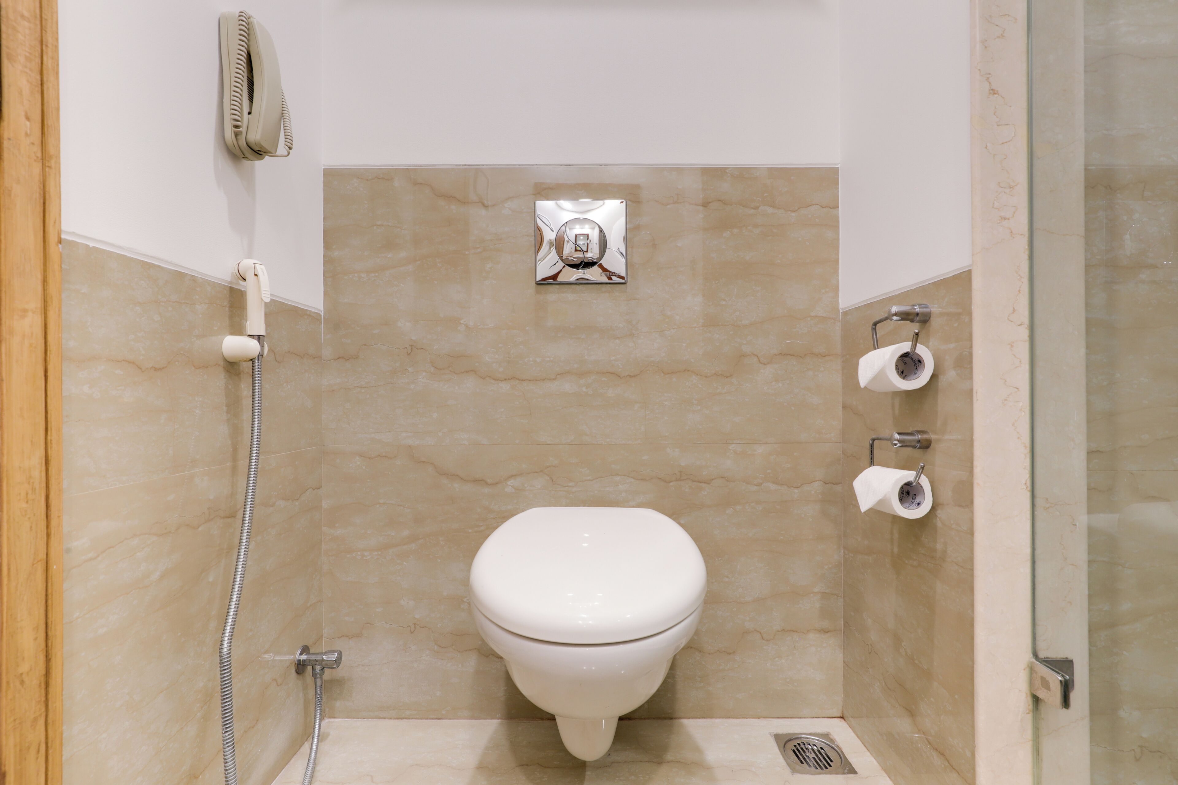 Uma casa de banho pequena com sanita, chuveiro, secador de mãos e suporte para papel higiénico.