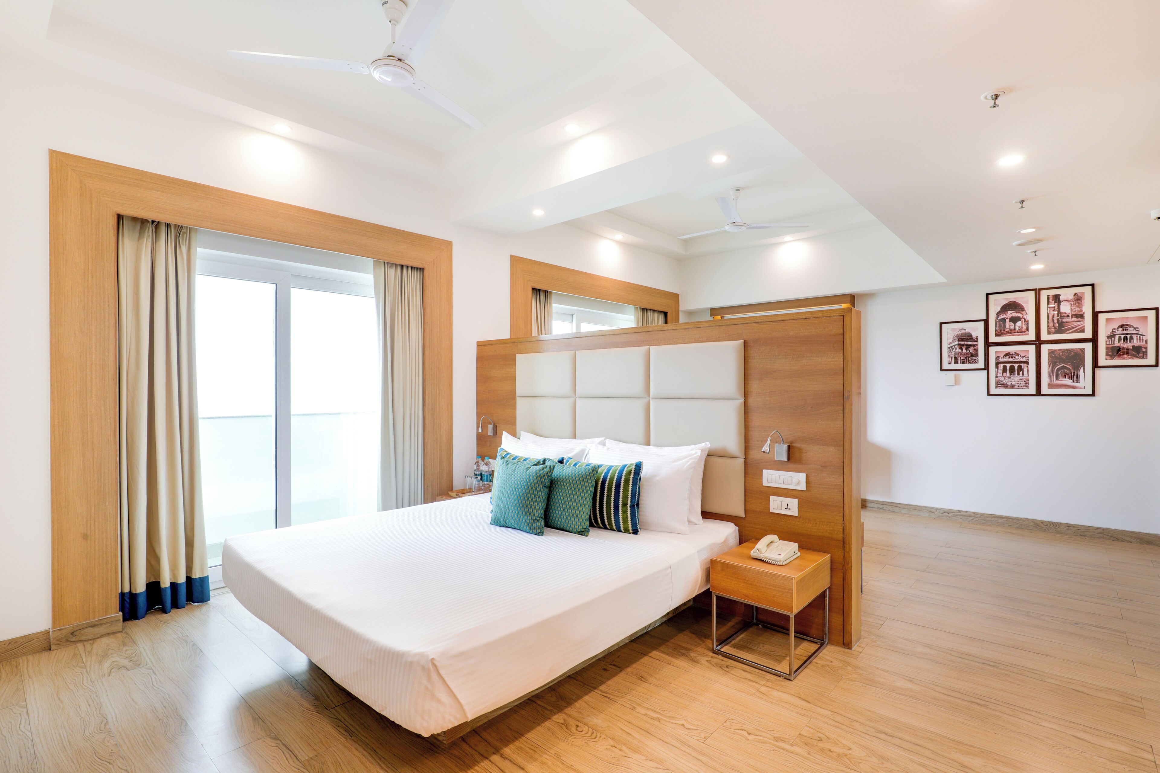 A hotel room with a large bed, a bedside table with a phone, and a wall with framed pictures.