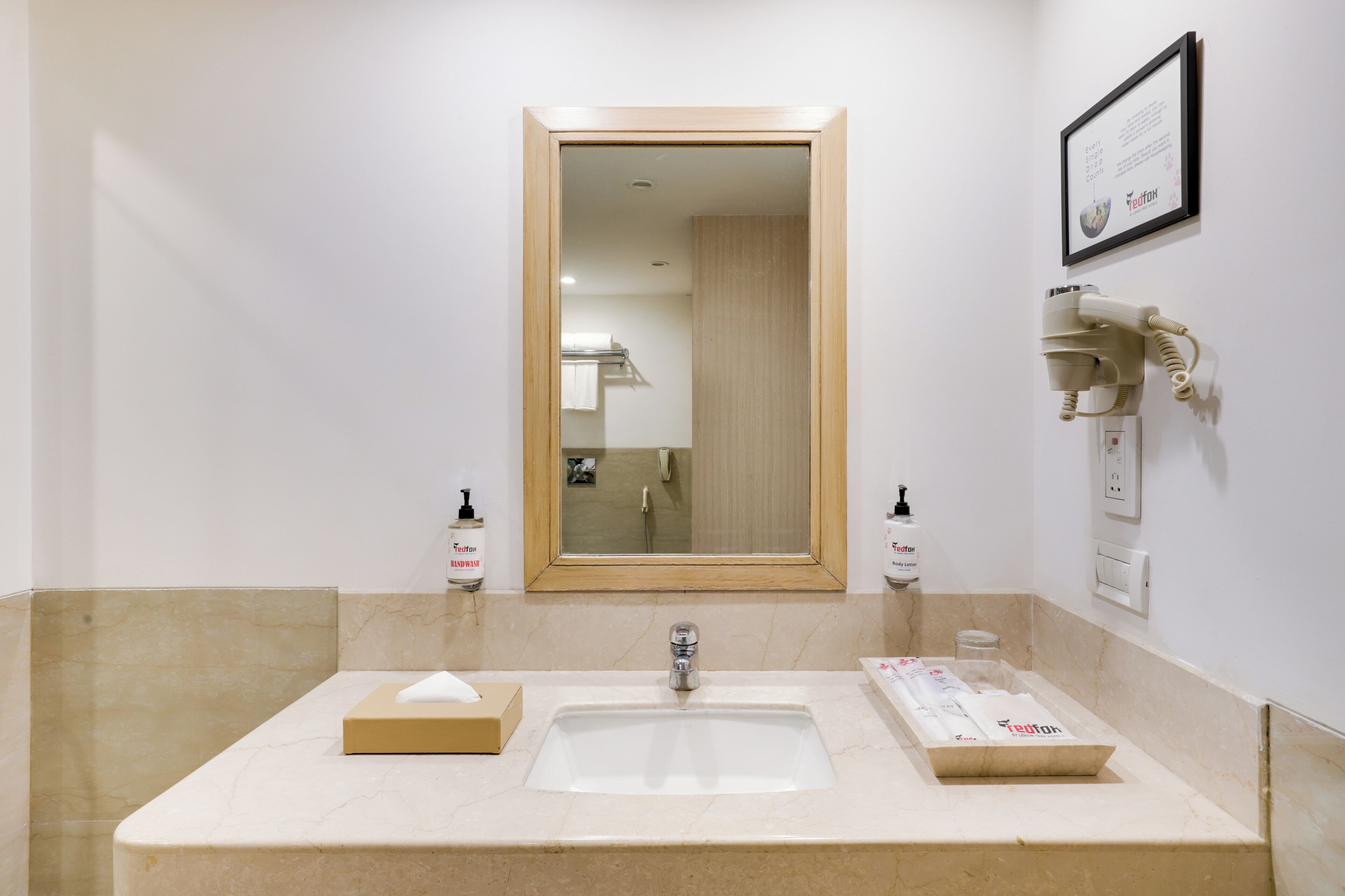 A bathroom with a sink, mirror, towel dispenser, and a framed informational sign.