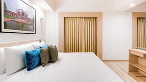 A hotel room with a bed, pillows, a desk, a chair, a large framed picture on the wall, and a window with curtains. - Red Fox by Lemon Tree Hotels, Sector 60, Gurugram (Sohna)