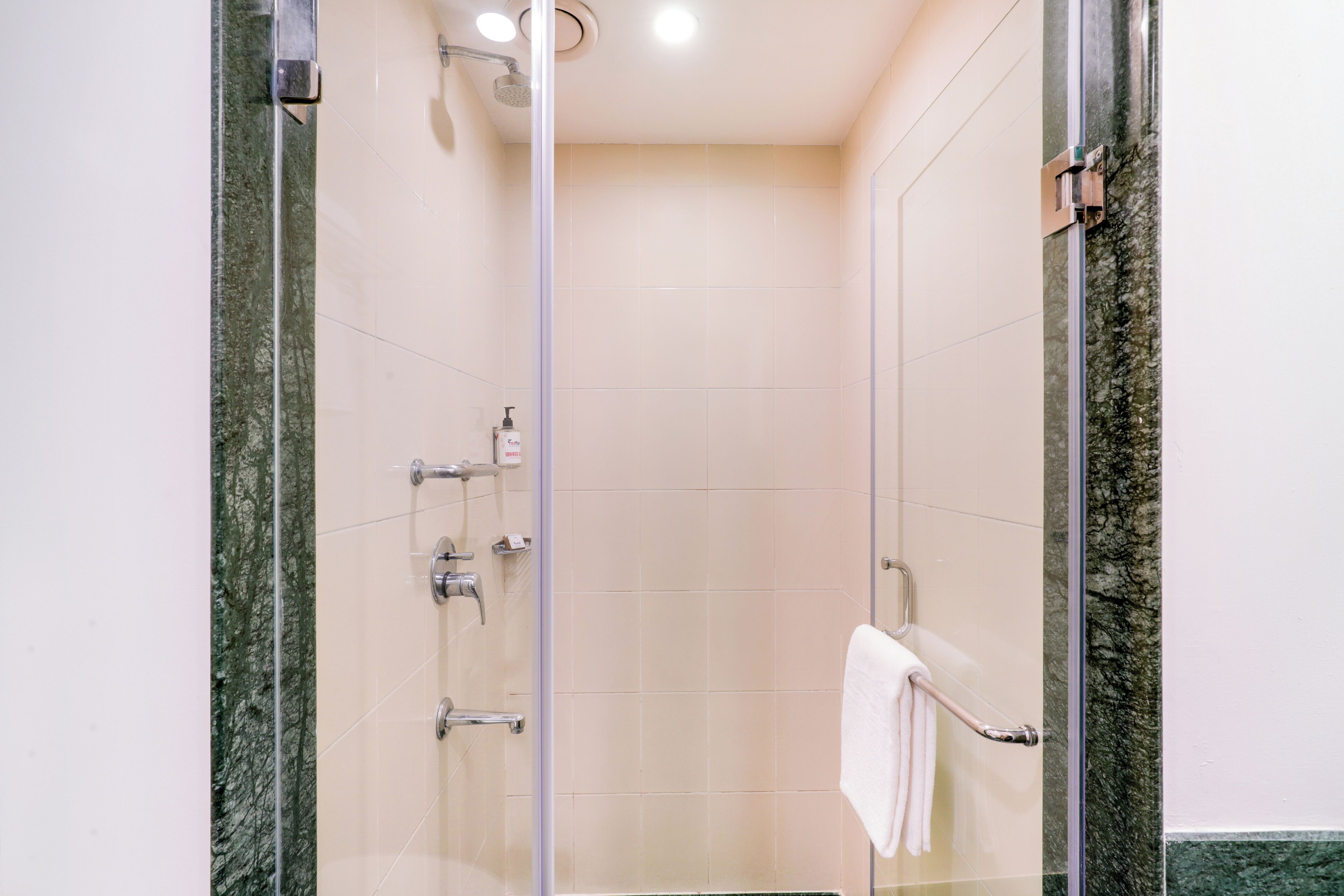 A glass-enclosed shower with a marble wall, a towel rack, and a visible showerhead.