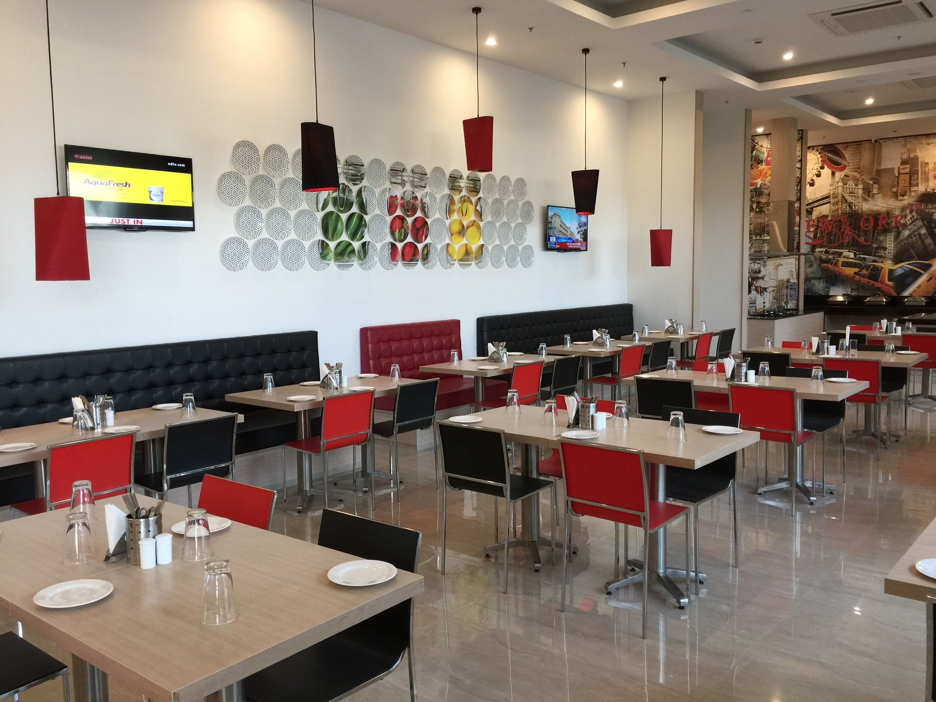 A restaurant with multiple tables and booths, a wall-mounted TV, and a patterned wall decoration.