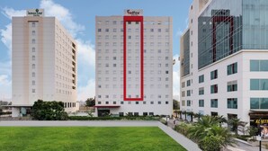 Three hotel buildings with a central red frame, surrounded by a well-maintained lawn and greenery. - Red Fox by Lemon Tree Hotels, Sector 60, Gurugram (Sohna)