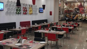 A restaurant with multiple tables and chairs, a wall-mounted TV, and a ceiling with recessed lighting. - Red Fox by Lemon Tree Hotels, Sector 60, Gurugram (Sohna)