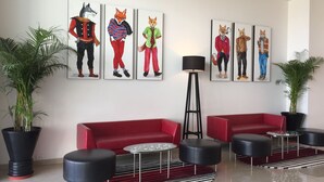 A modern lobby with red sofas, black ottomans, and a striped rug. There are six animal-themed paintings on the wall. - Red Fox by Lemon Tree Hotels, Sector 60, Gurugram (Sohna)