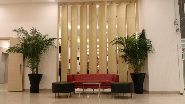 A lobby with a red sofa, two black armchairs, and two large potted plants. - Red Fox by Lemon Tree Hotels, Sector 60, Gurugram (Sohna)