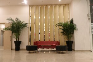 Un vestíbulo con un sofá rojo, dos sillones negros y dos grandes macetas con plantas.