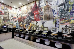 Un espace buffet comprenant plusieurs stands de restauration et un mur décoré de fresques représentant des paysages urbains.