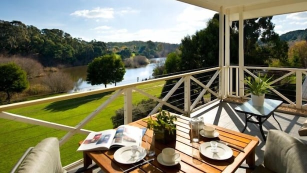 Un balcón con una mesa dispuesta para dos personas, con vistas a un río y follaje.