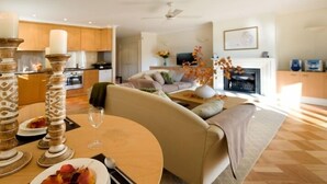 Una sala de estar moderna con un sofá color beige, una mesa de comedor con un florero y platos, y una cocina al fondo.