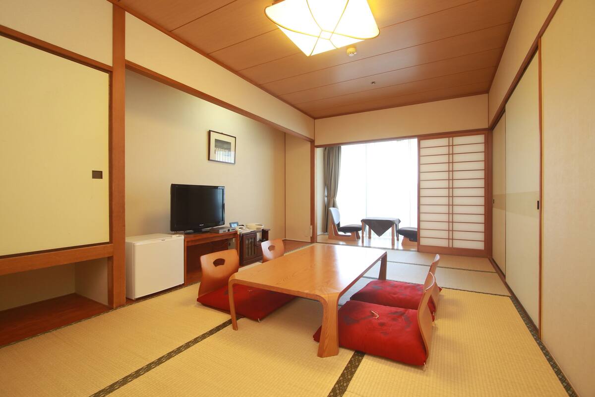 Una habitación japonesa tradicional con suelo de tatami, una mesa baja y cojines rojos.