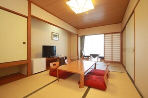A traditional Japanese room with tatami flooring, a low table, and red cushions.