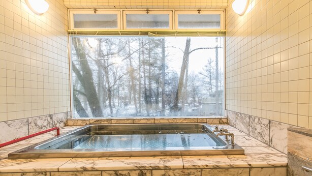 Un baño con una bañera grande, paredes de mármol y una ventana que da a un bosque.