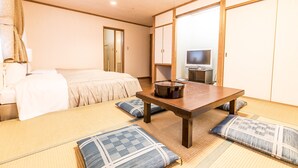 Una habitación tradicional japonesa con suelo de tatami, una mesa baja de madera y una cama con colcha blanca.