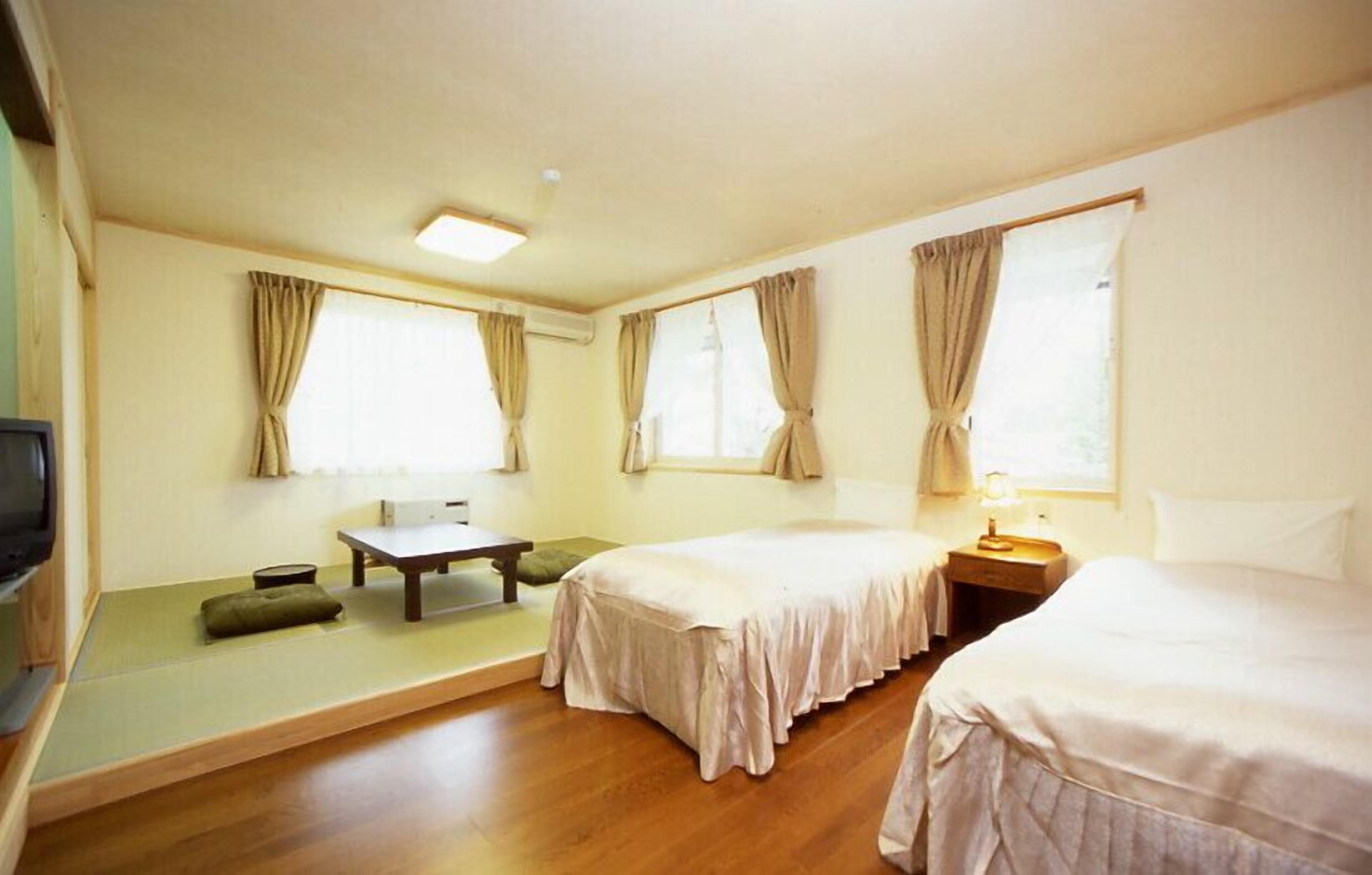 Quarto de hotel com duas camas, uma mesa pequena, um sofá e uma televisão.