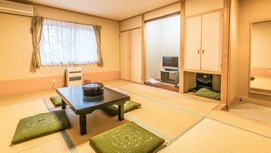 Una habitación japonesa tradicional con suelo de tatami, una mesa baja de tatami con cojines, puertas correderas y un televisor.