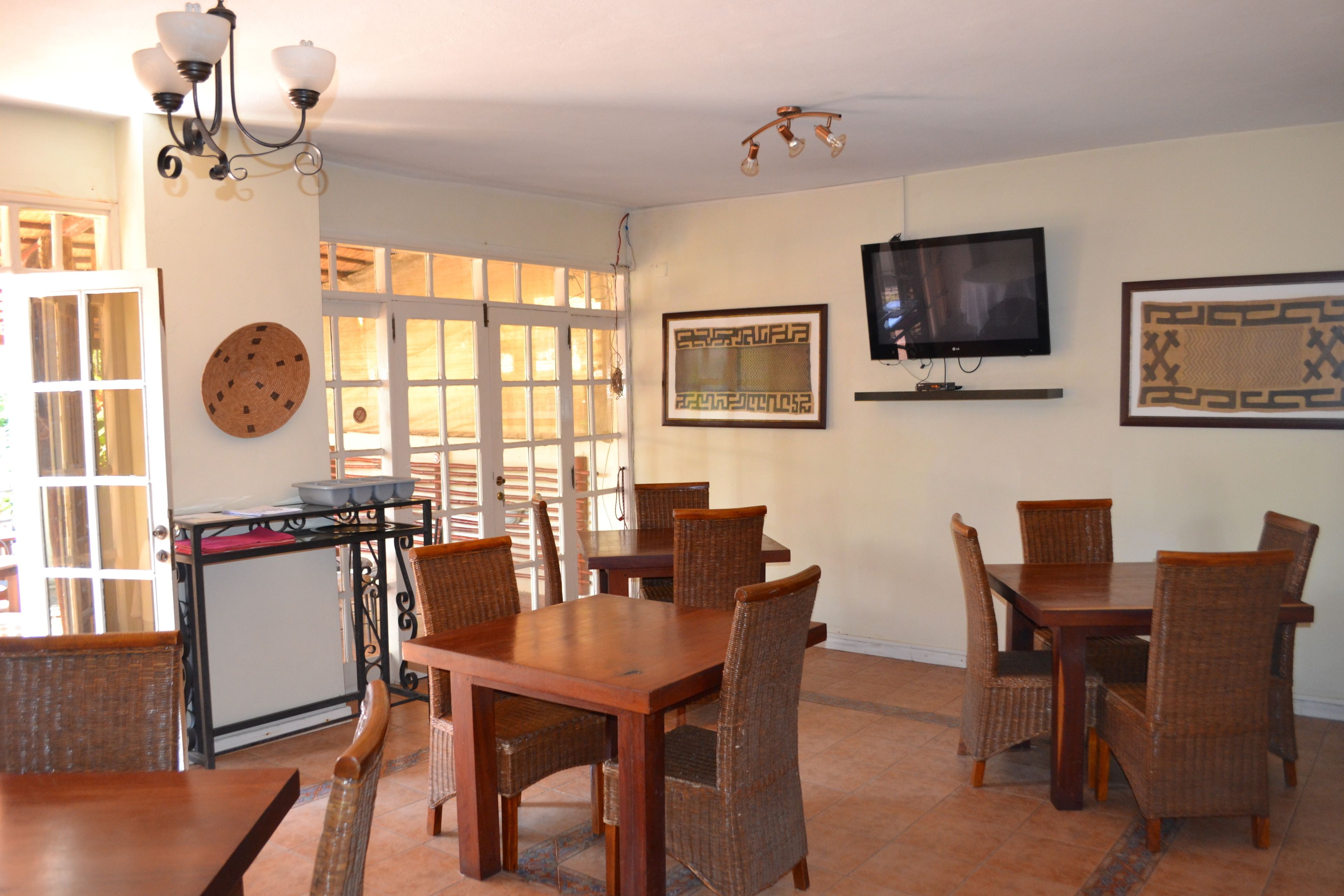 A dining area with a wooden table and wicker chairs, a television mounted on the wall, and a decorative wall hanging.