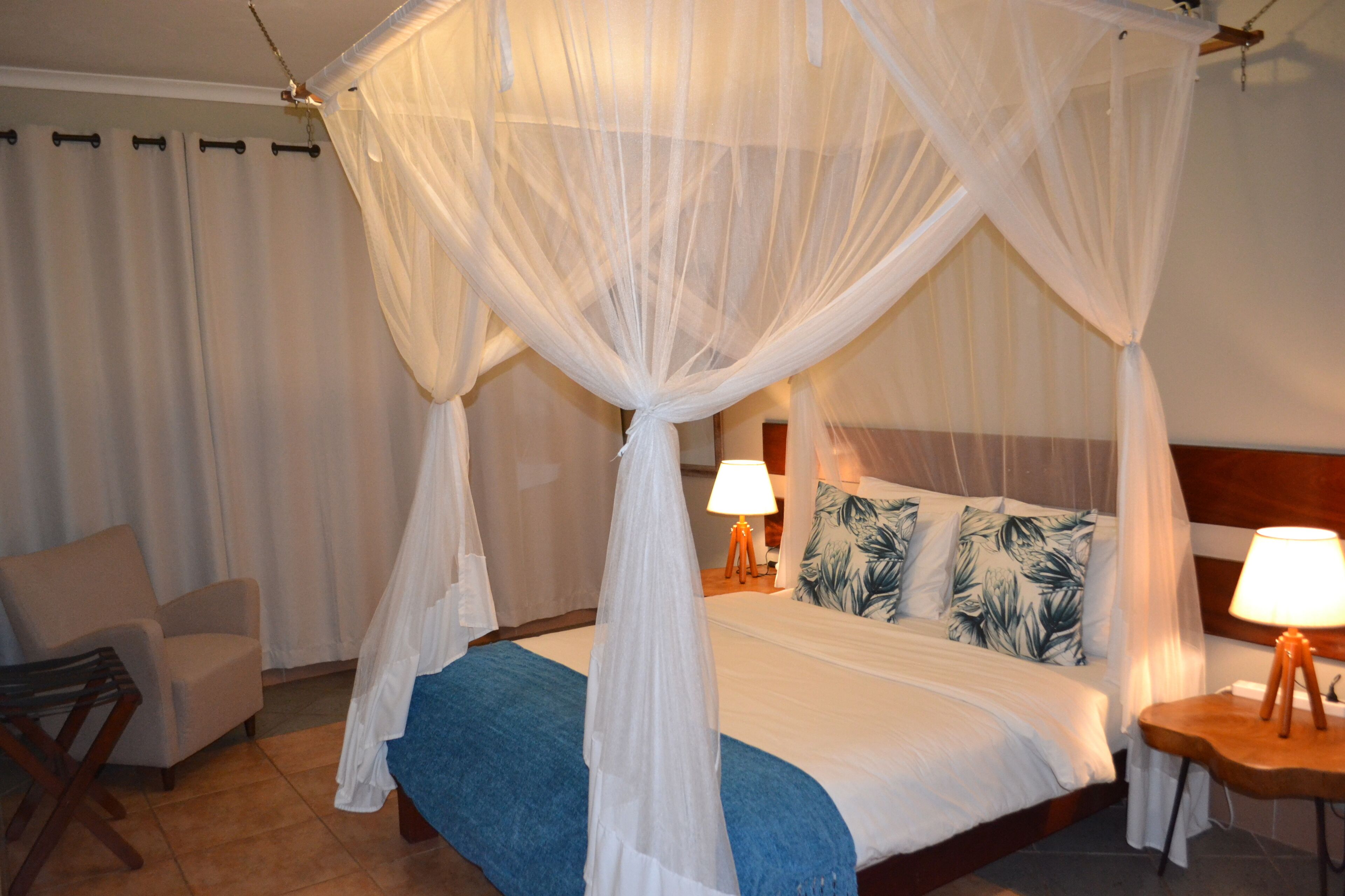 Una habitación de hotel con una cama con dosel, una silla y dos lámparas de noche.