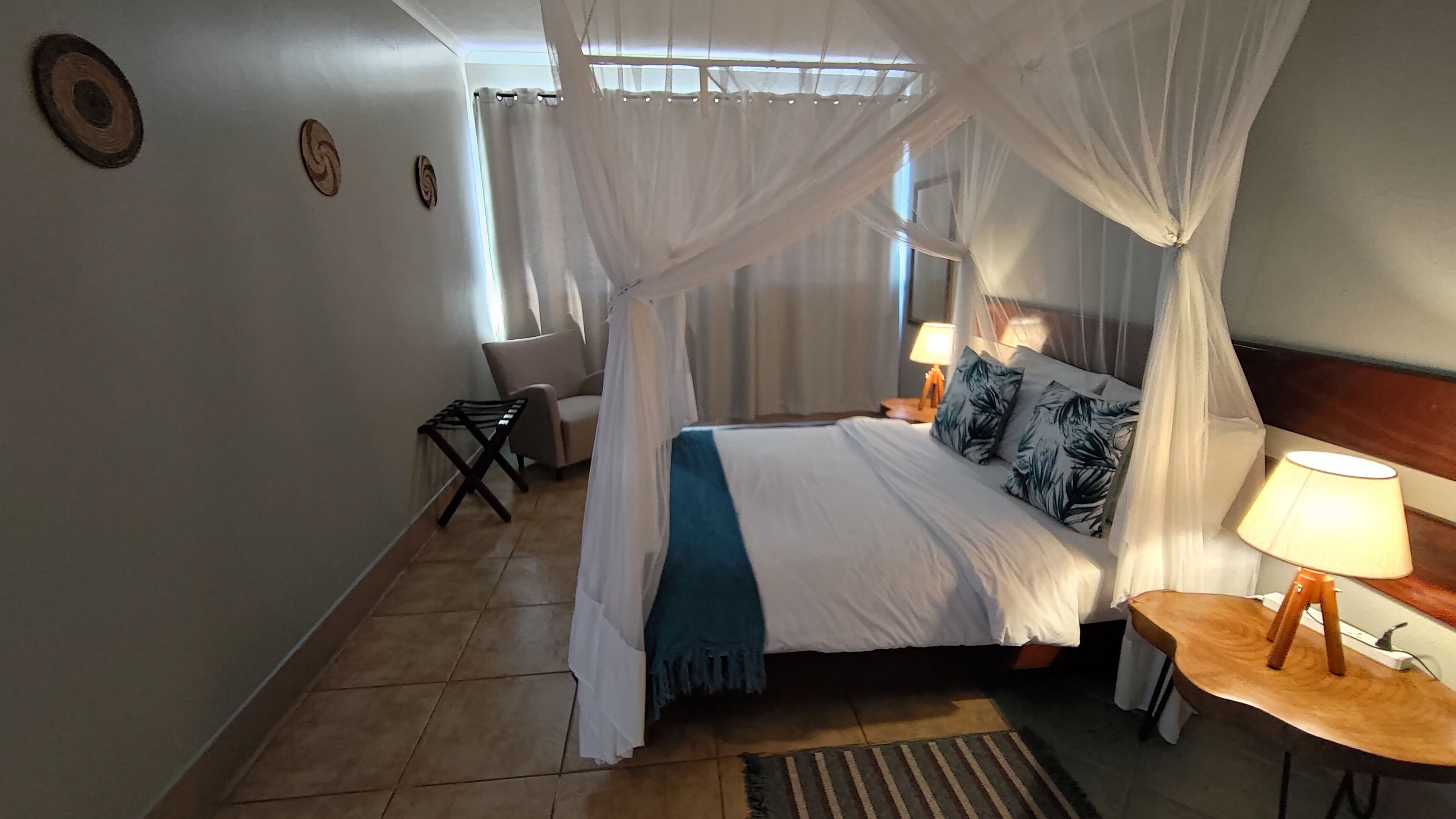 A bedroom with a bed under a canopy, a bedside table with a lamp, and a chair.