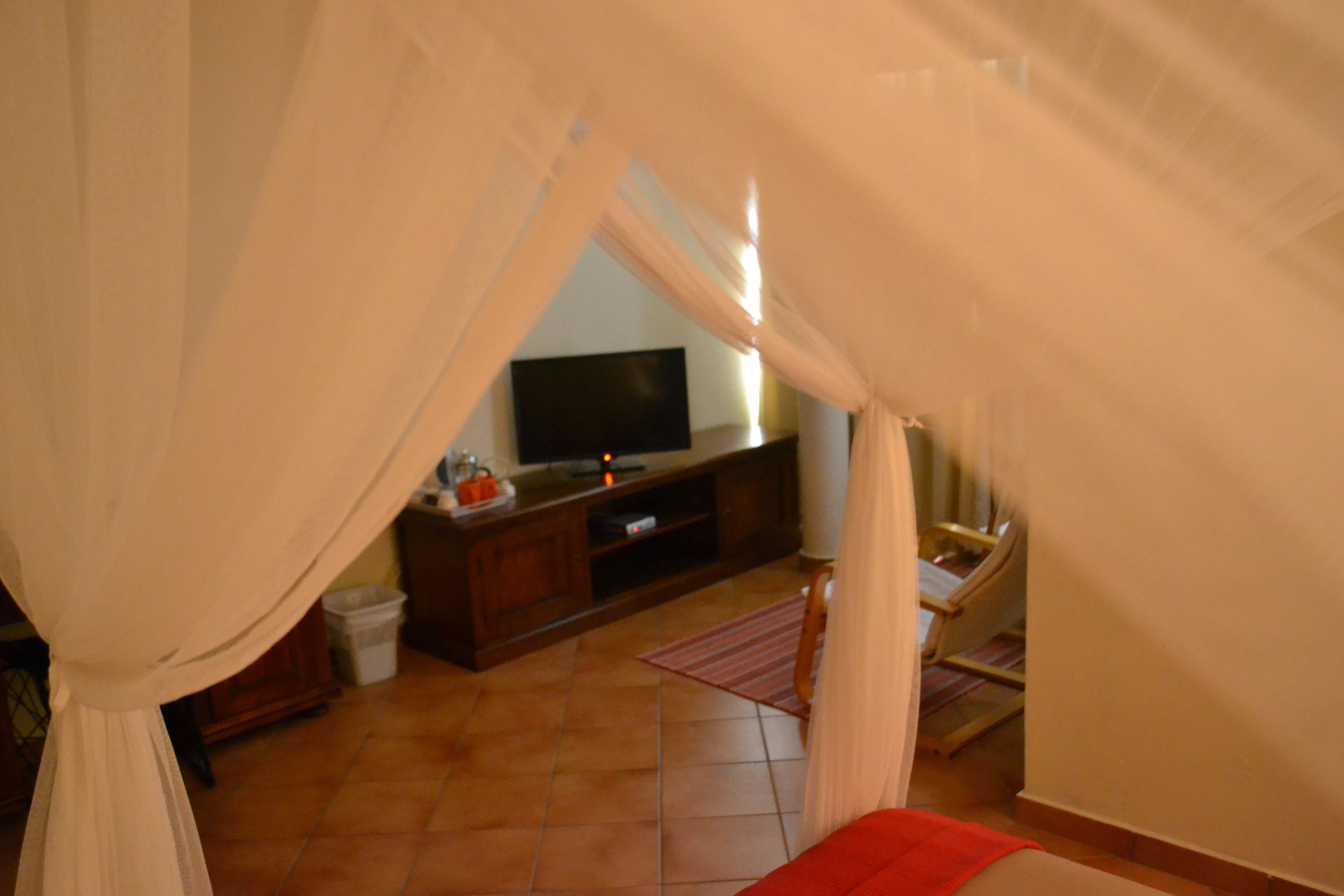 Una habitación con televisión sobre un mueble de madera, una silla y una cama con manta roja.