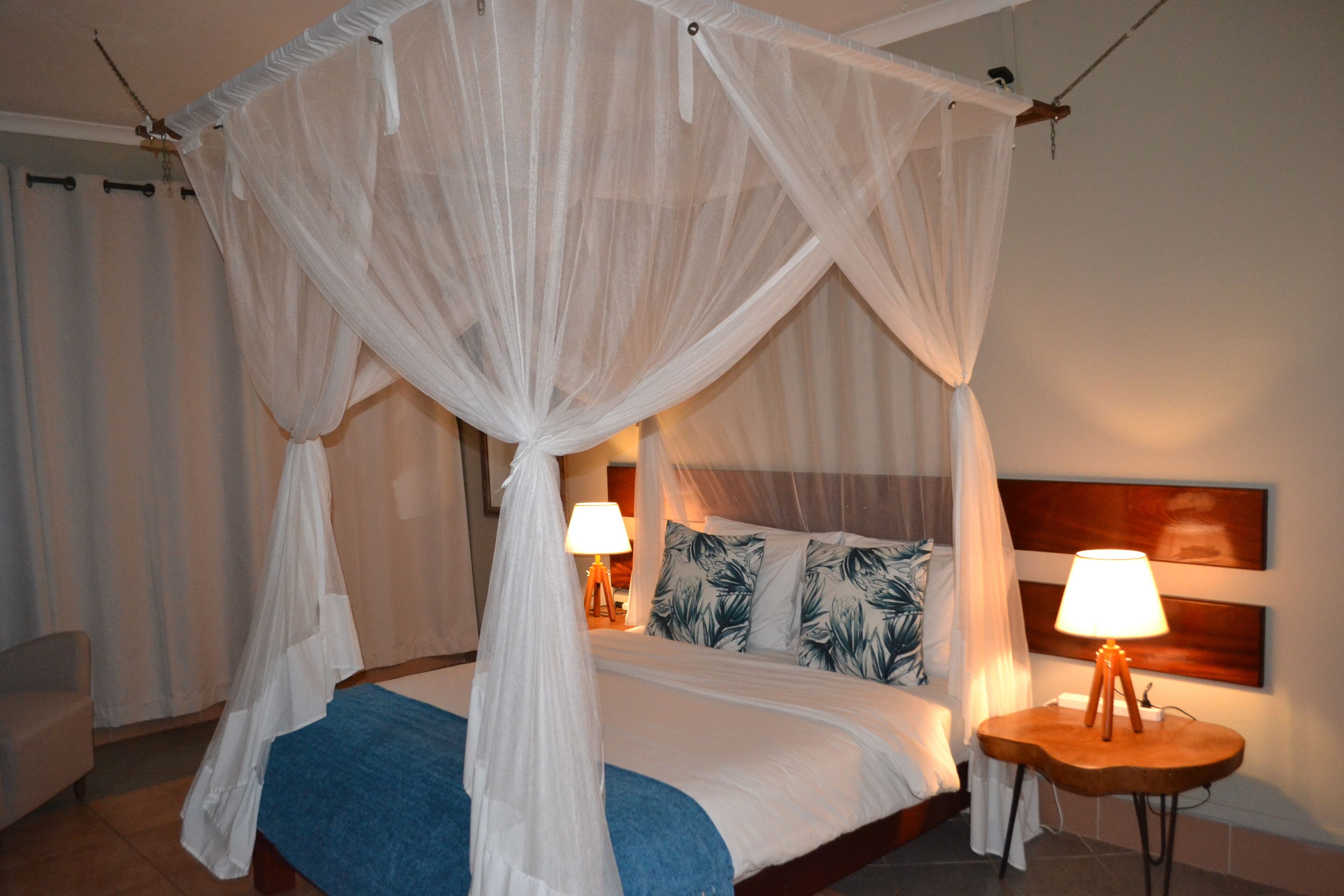 A bedroom with a four-poster canopy bed, a bedside table with a lamp, and a headboard with a wooden panel.