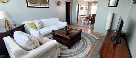 A living room with a white sofa, a wooden coffee table, and a television on a stand.