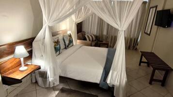 A bedroom with a four-poster canopy bed, a bedside table with a lamp, a bench, and a small rug.