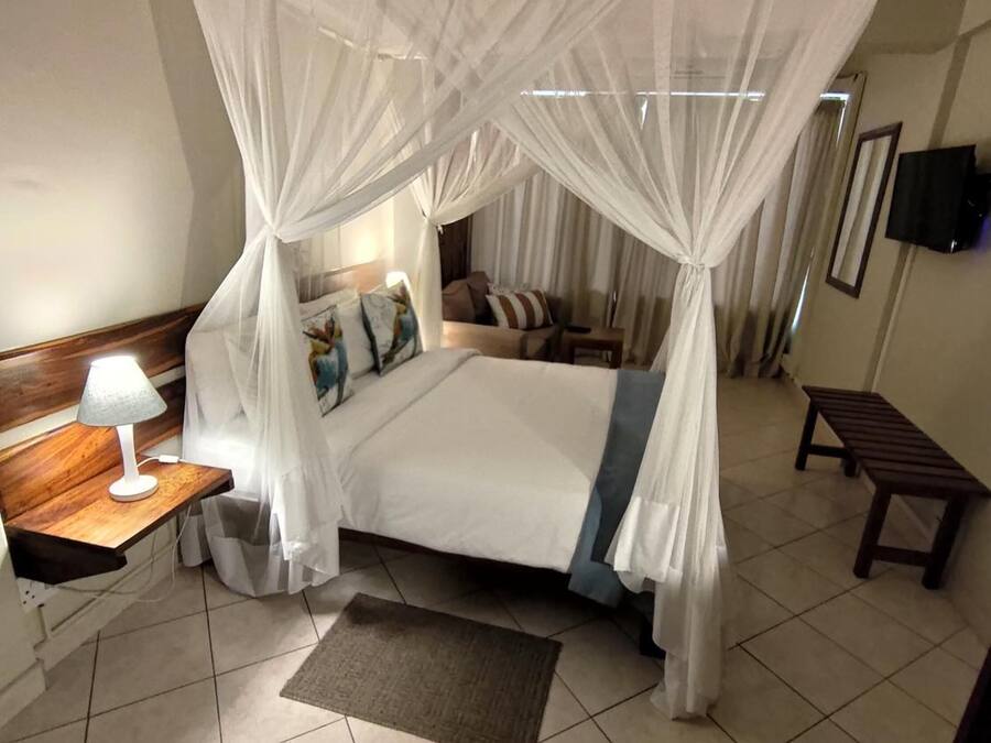 A bedroom with a four-poster canopy bed, a bedside table with a lamp, a bench, and a small rug.